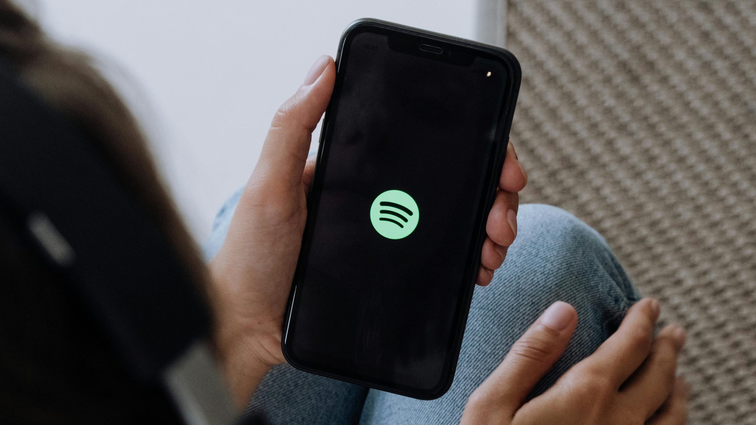 A person listening to music with headphones and smartphone, displaying Spotify logo.